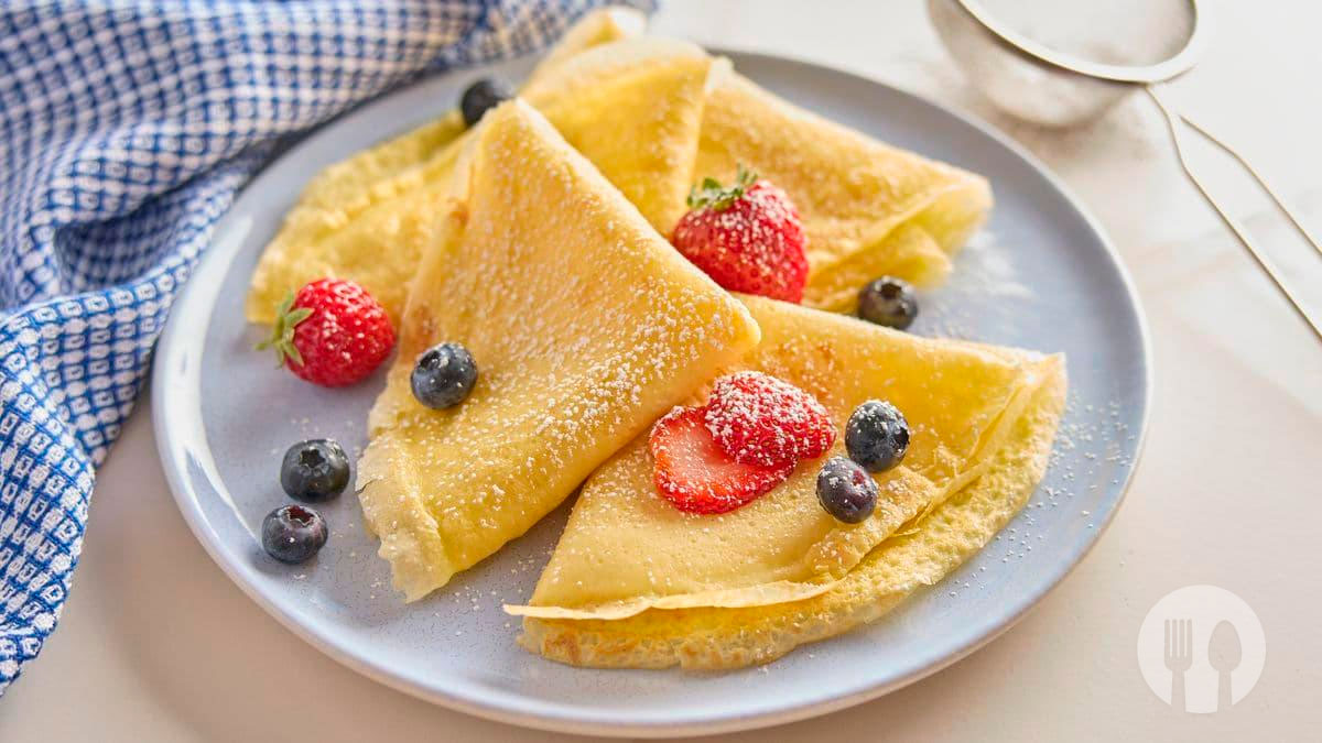 Crepes caseiros simples, finos e macios, ligeiramente dourados, servidos com morangos frescos e açúcar em pó, perfeitos para o pequeno-almoço ou lanche.